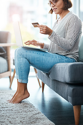 Buy stock photo Cropped shot of a young woman using her laptop and credit card on the sofa at home
