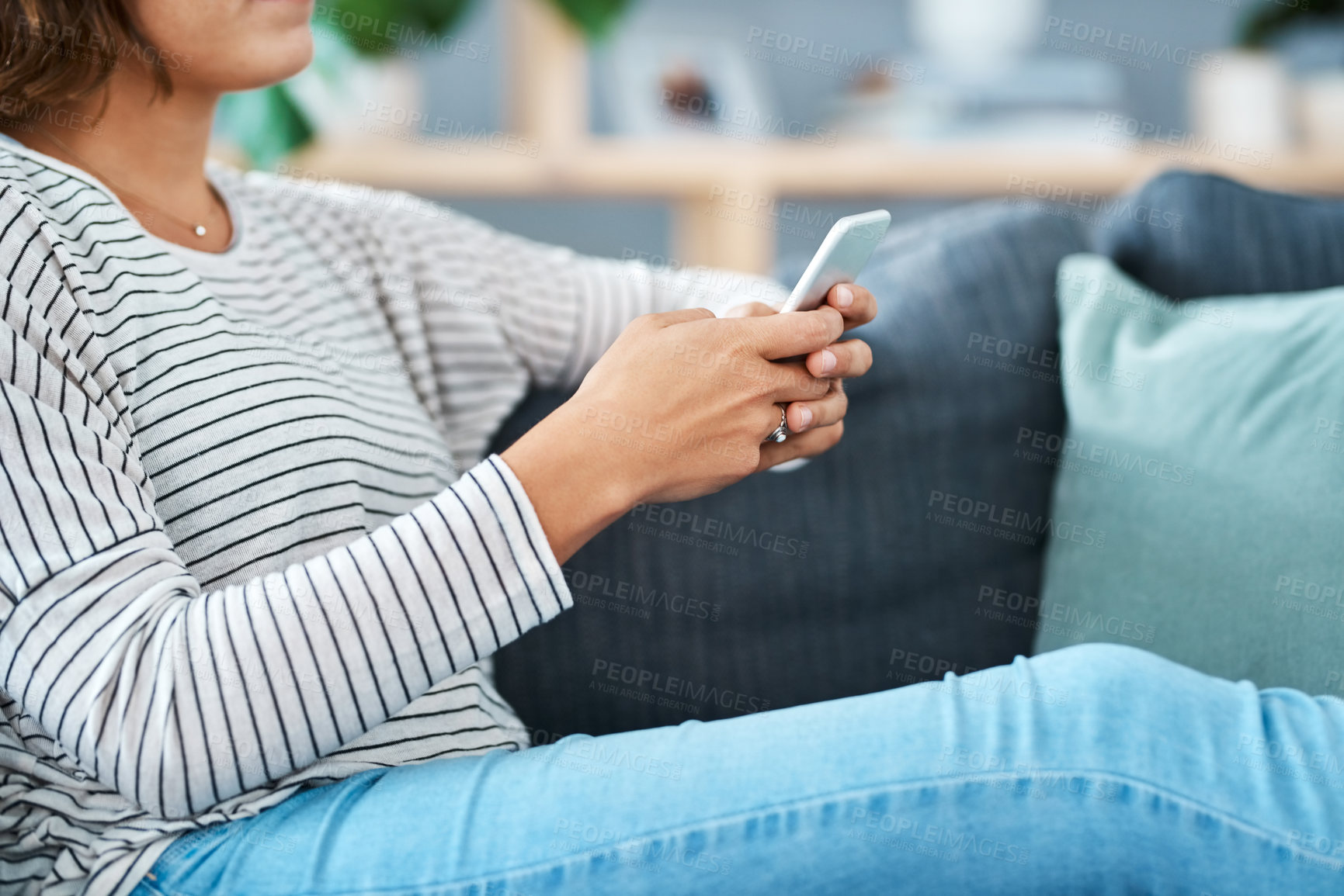 Buy stock photo Cropped shot of a young woman using her smartphone on the sofa at home