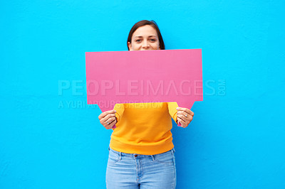 Buy stock photo Cropped portrait of a young woman holding a speech bubble against a blue background