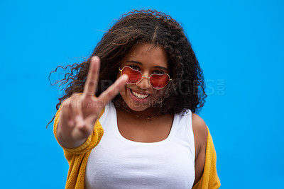 Buy stock photo Cropped portrait of an attractive young woman showing the peace sign against a blue background