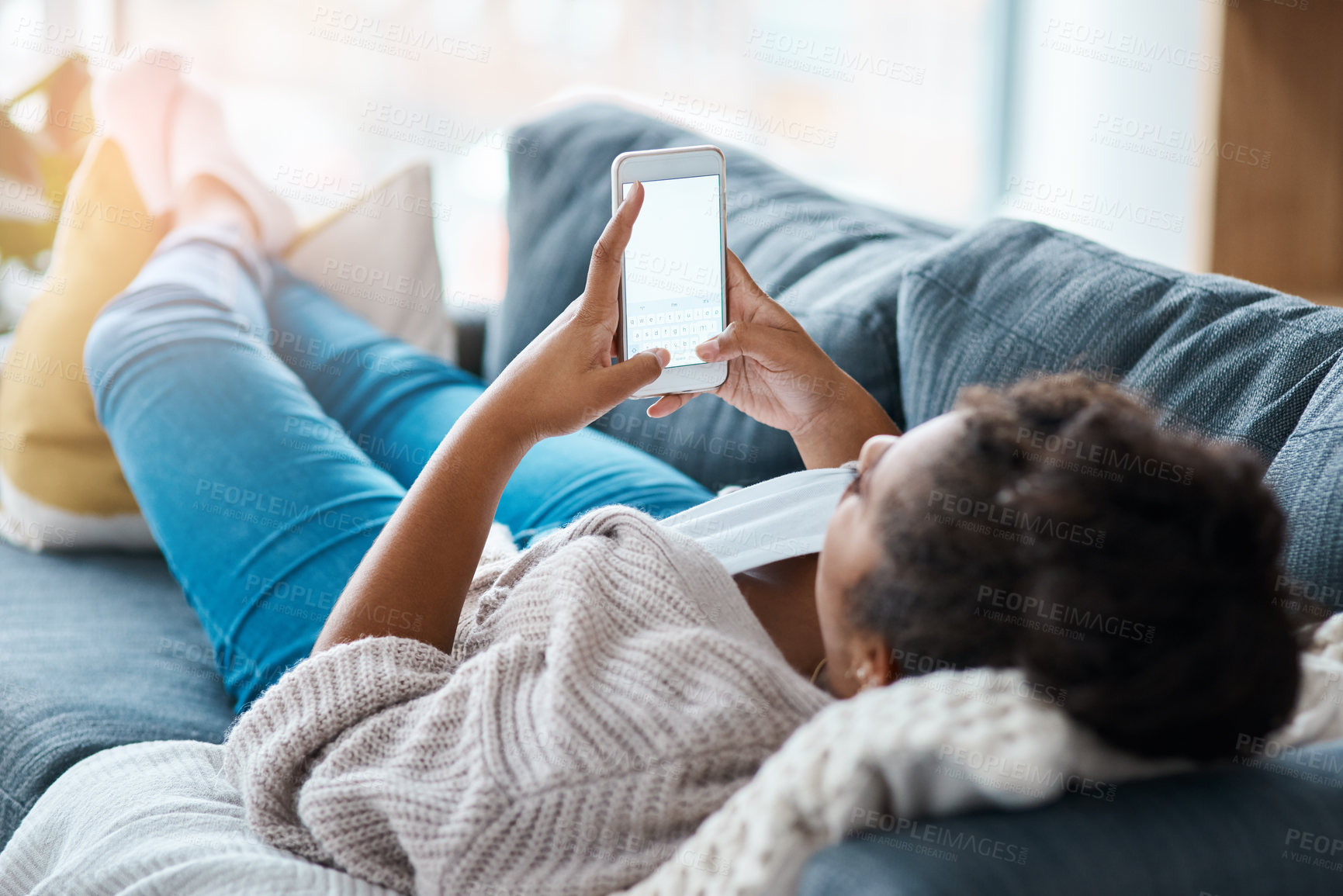 Buy stock photo Full length shot of an unrecognizable woman using her smartphone while lying on the sofa