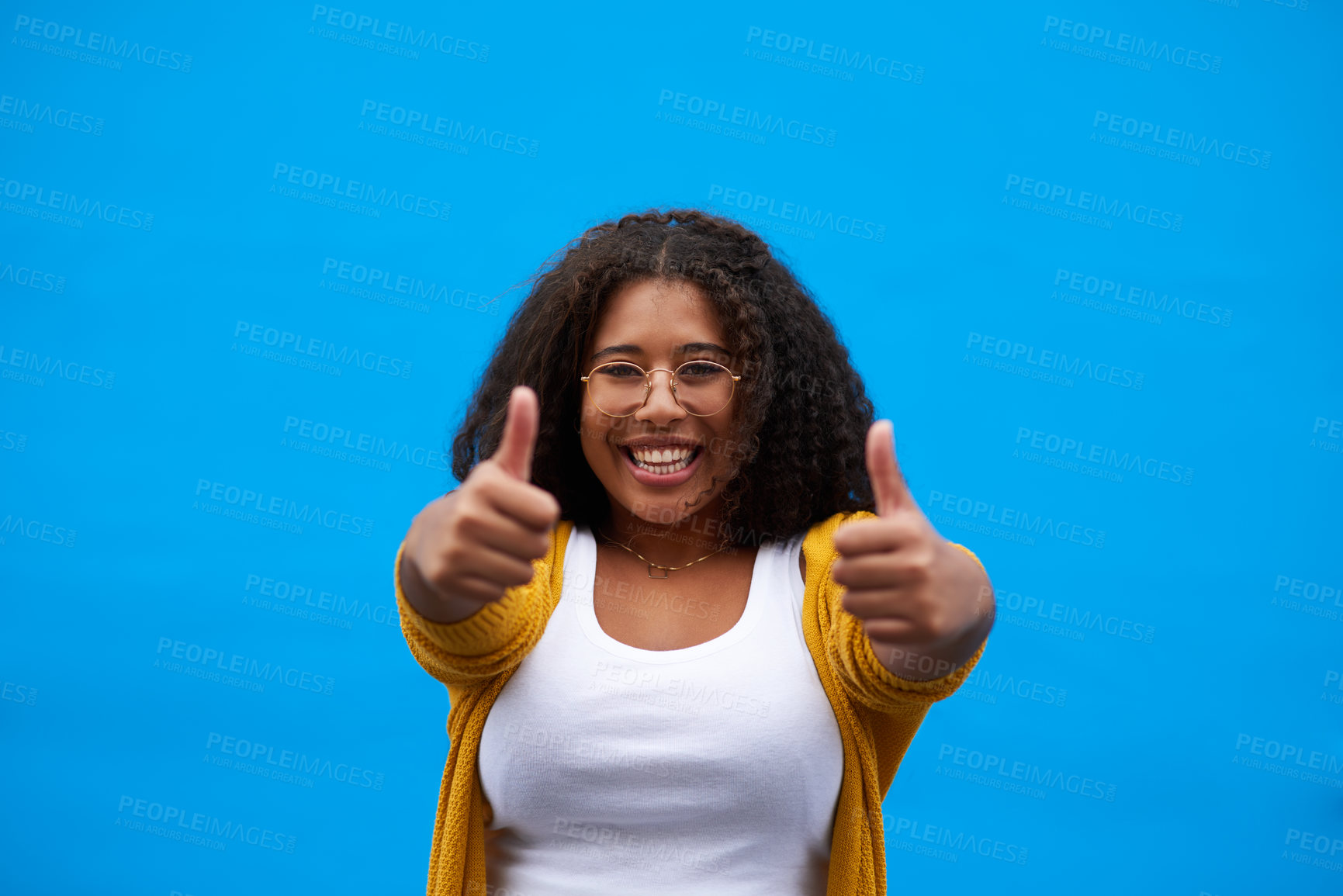 Buy stock photo Cropped portrait of an attractive young woman showing thumbs up against a blue background