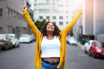 Buy stock photo Cropped shot of a happy young woman celebrating with arms raised against a city background