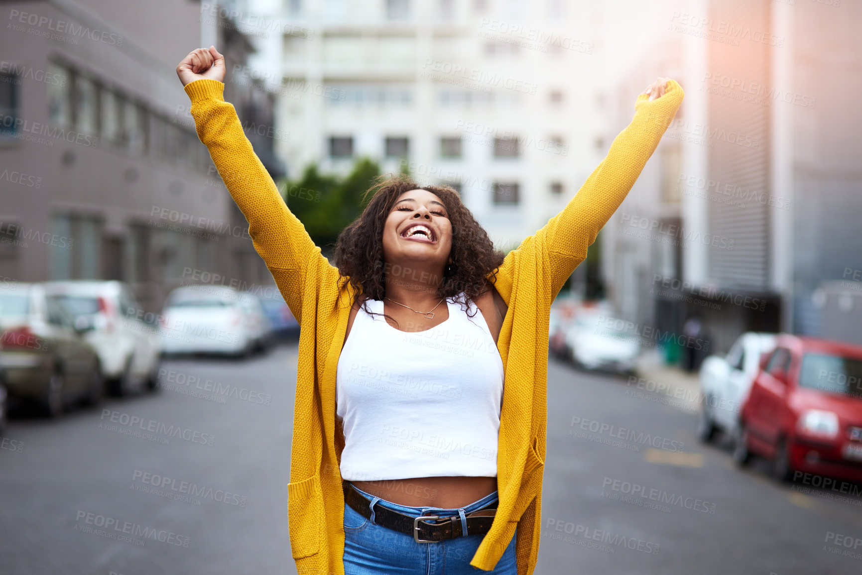 Buy stock photo Cropped shot of a happy young woman celebrating with arms raised against a city background