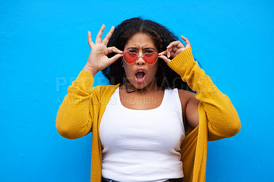 Buy stock photo Cropped portrait of an attractive young woman adjusting her sunglasses against a blue background