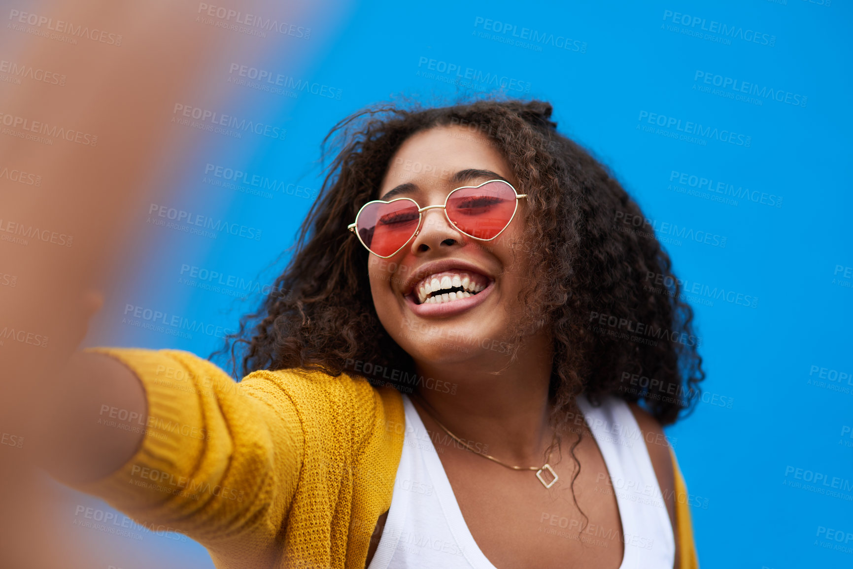 Buy stock photo Cropped portrait of a happy young woman taking a selfie against a blue background