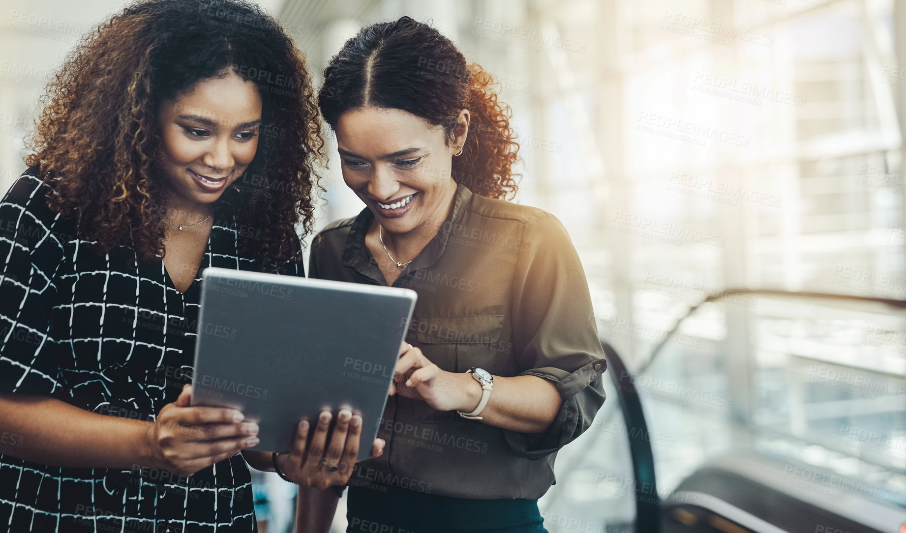 Buy stock photo Cropped shot of two attractive businesswomen using a digital tablet together while standing in a modern workplace