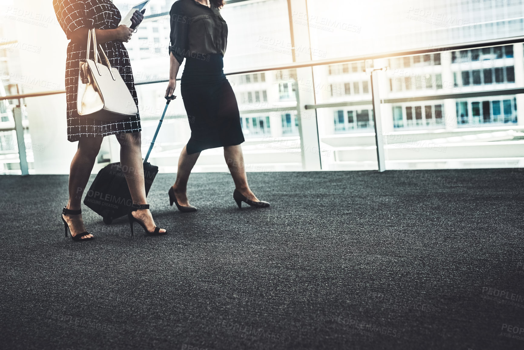 Buy stock photo Cropped shot of two unrecognizable businesswomen walking together with their bags in a modern workplace