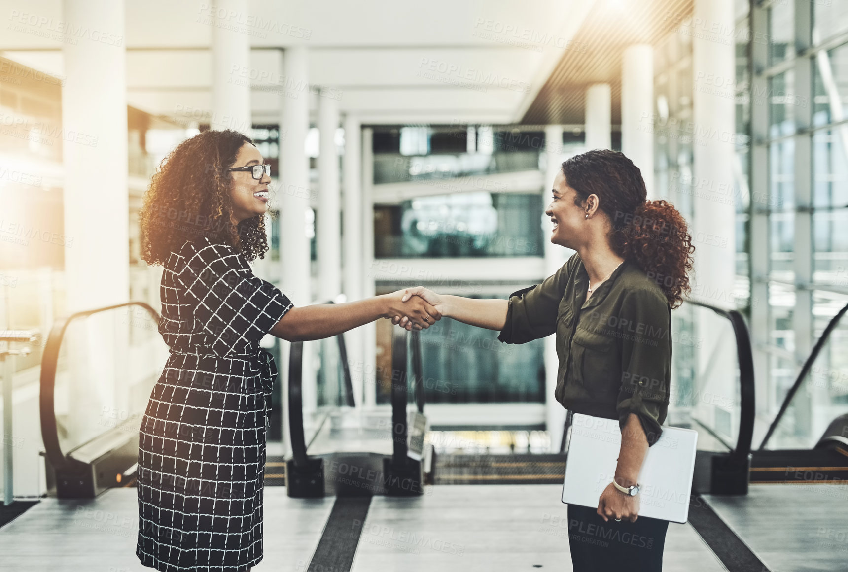 Buy stock photo Shot of two attractive businesswomen shaking hands in the workplace