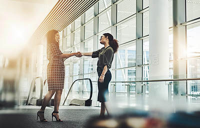 Buy stock photo Full length shot of two attractive young businesswomen shaking hands while standing in a modern workplace