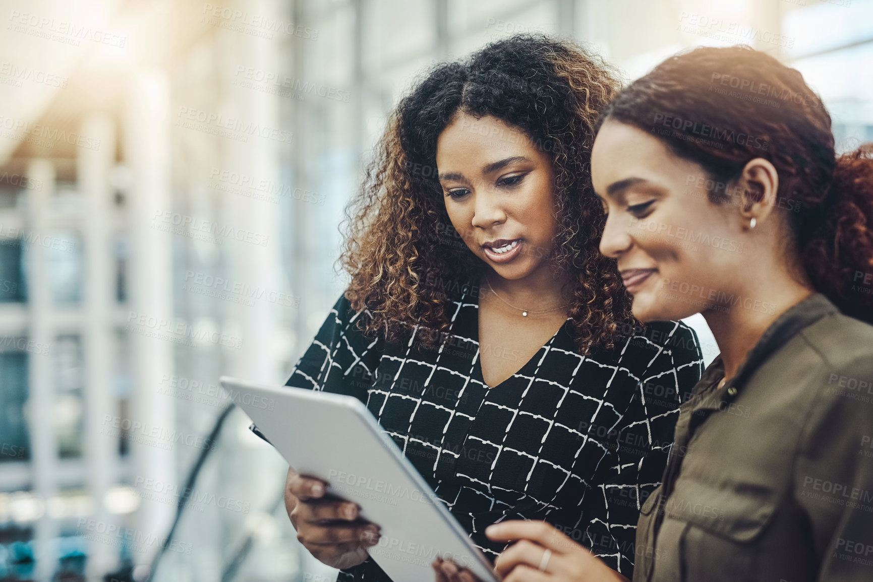 Buy stock photo Cropped shot of two attractive businesswomen using a digital tablet together while standing in a modern workplace