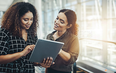 Buy stock photo Cropped shot of two attractive businesswomen using a digital tablet together while standing in a modern workplace