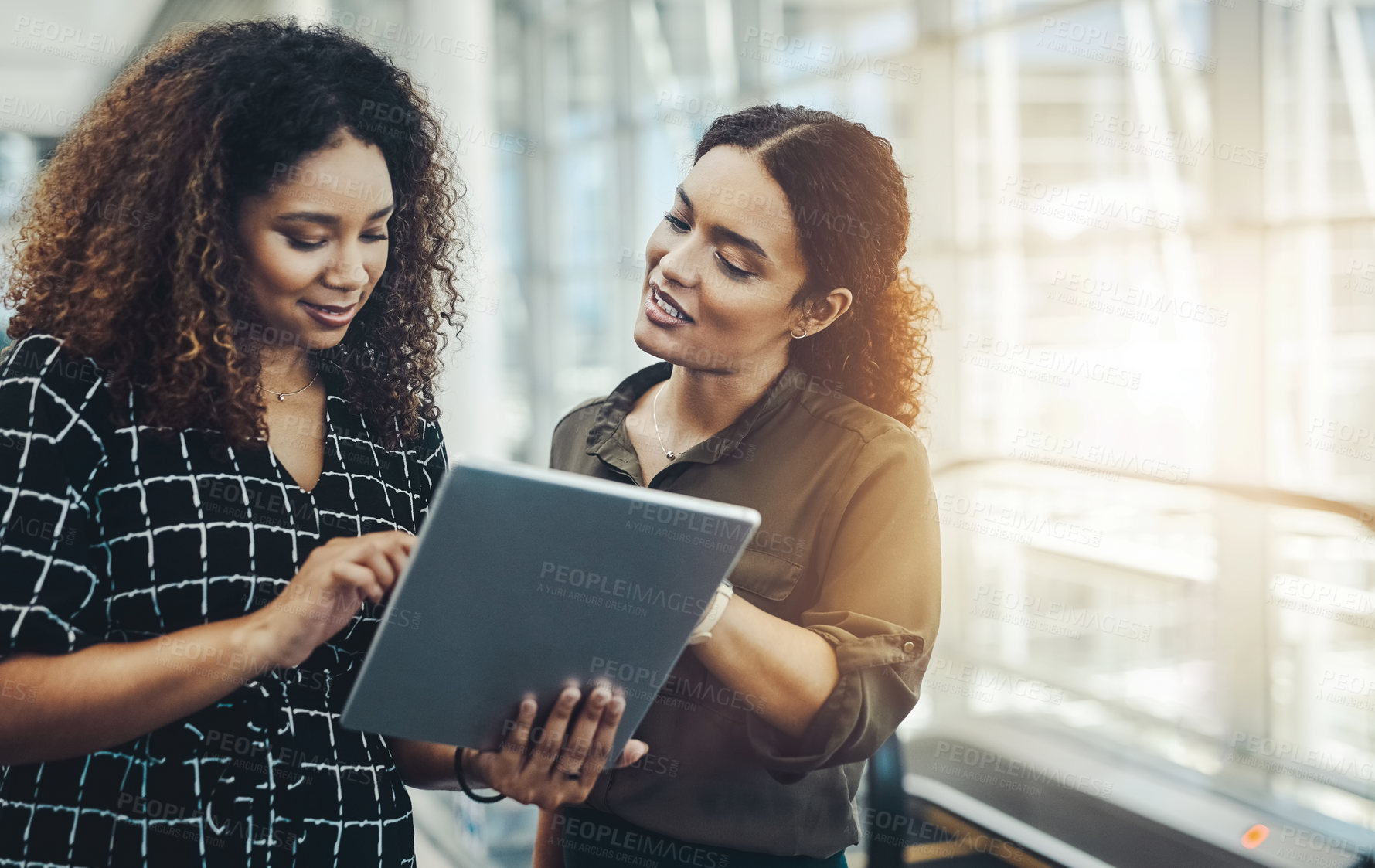 Buy stock photo Cropped shot of two attractive businesswomen using a digital tablet together while standing in a modern workplace