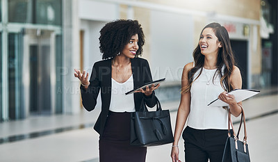 Buy stock photo Cropped shot of two young businesswomen walking together while holding digital tablets at work during the day