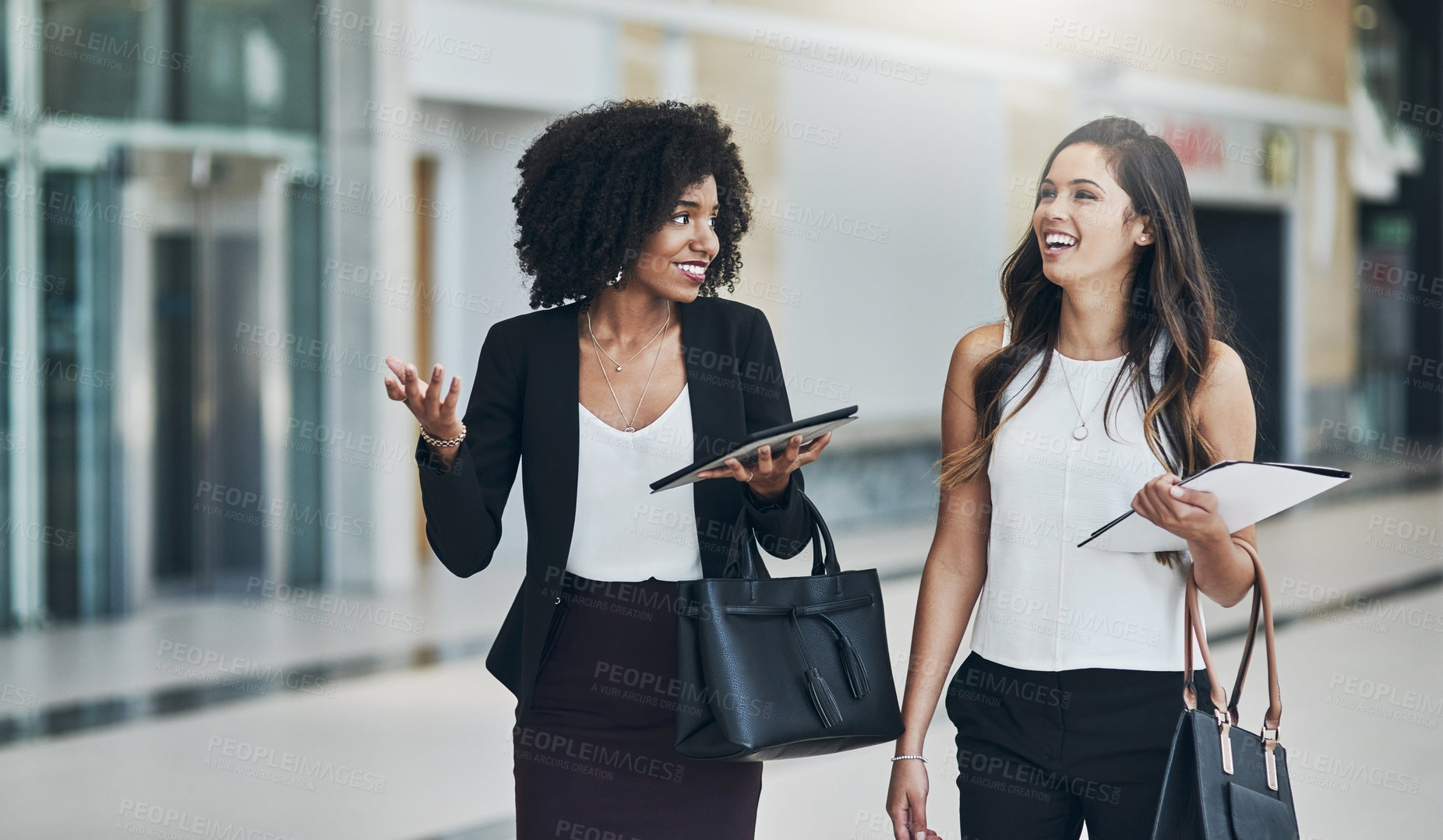 Buy stock photo Cropped shot of two young businesswomen walking together while holding digital tablets at work during the day