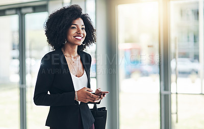 Buy stock photo Shot of a confident young businesswoman texting on her phone while standing in the office at work