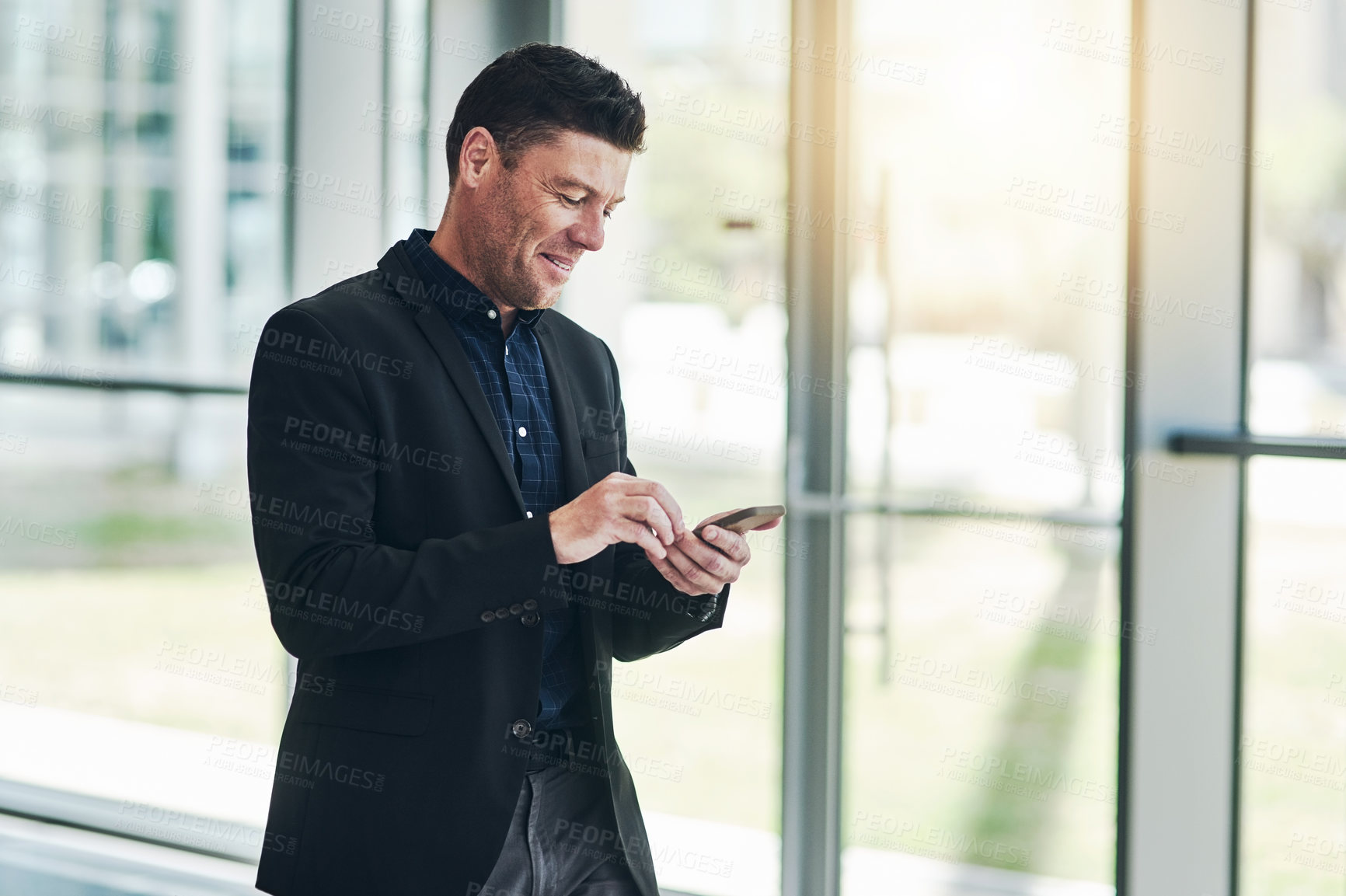 Buy stock photo Shot of a confident young businessman texting on his phone while standing in the office at work