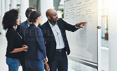 Buy stock photo Shot of a group of confident businesspeople having a meeting while explaining on a white board inside of the office