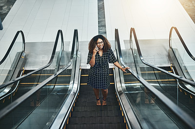 Buy stock photo High angle shot of an attractive young businesswoman taking a phonecall while going up an escalator in a modern office