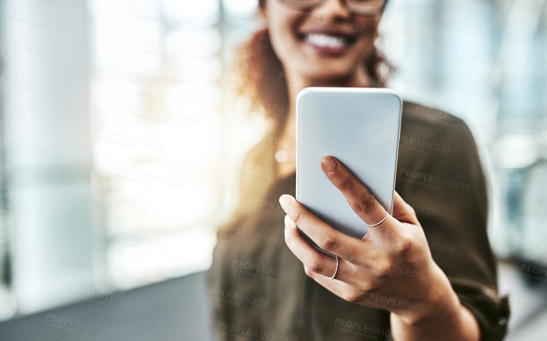 Buy stock photo Cropped shot of an unrecognizable businesswoman using a smartphone while standing in a modern office