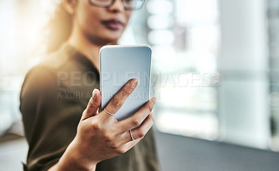 Buy stock photo Cropped shot of an unrecognizable businesswoman using a smartphone while standing in a modern office