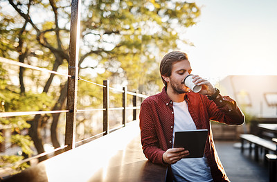 Buy stock photo Cropped shot of a handsome young man using his digital tablet while drinking coffee outside