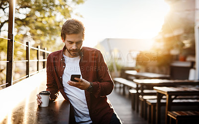 Buy stock photo Cropped shot of a handsome young man using his cellphone while drinking coffee outside