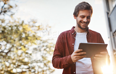 Buy stock photo Cropped shot of a handsome young man using his digital tablet outside