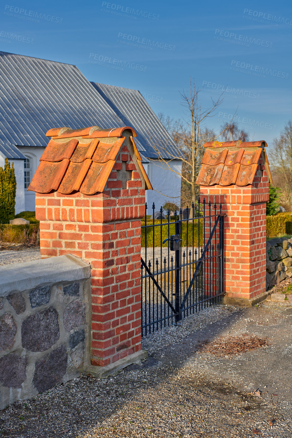 Buy stock photo A closed black iron gate between two red brick pillars at a park on a sunny summer day. Outdoor entrance to a home or house in a small town or village with a blue sky in the background
