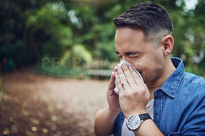 Buy stock photo Cropped shot of a young man blowing his nose with a tissue outdoors