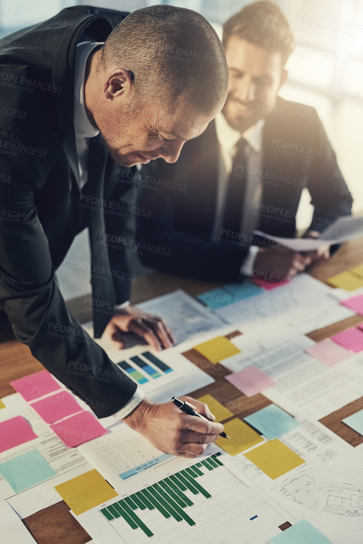 Buy stock photo Cropped shot of two businessmen going over paperwork during a meeting in their office