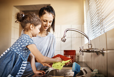 Buy stock photo Shot of a happy little girl and her mother washing the dishes together at home