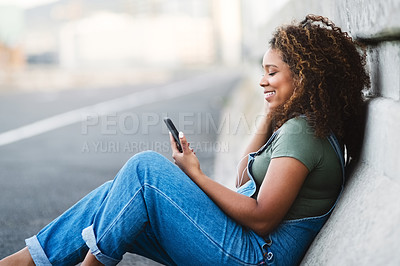 Buy stock photo Shot of an attractive young woman sitting down and listening to music on her cellphone in the city