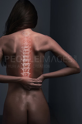 Buy stock photo Rearview shot of a naked young woman suffering from lower back pain against a dark background