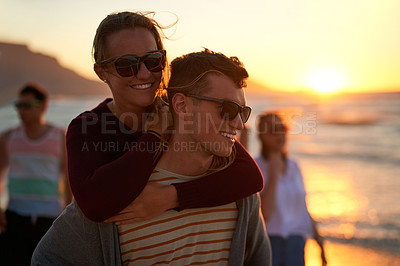 Buy stock photo Cropped shot of an affectionate young man piggybacking his girlfriend on the beach
