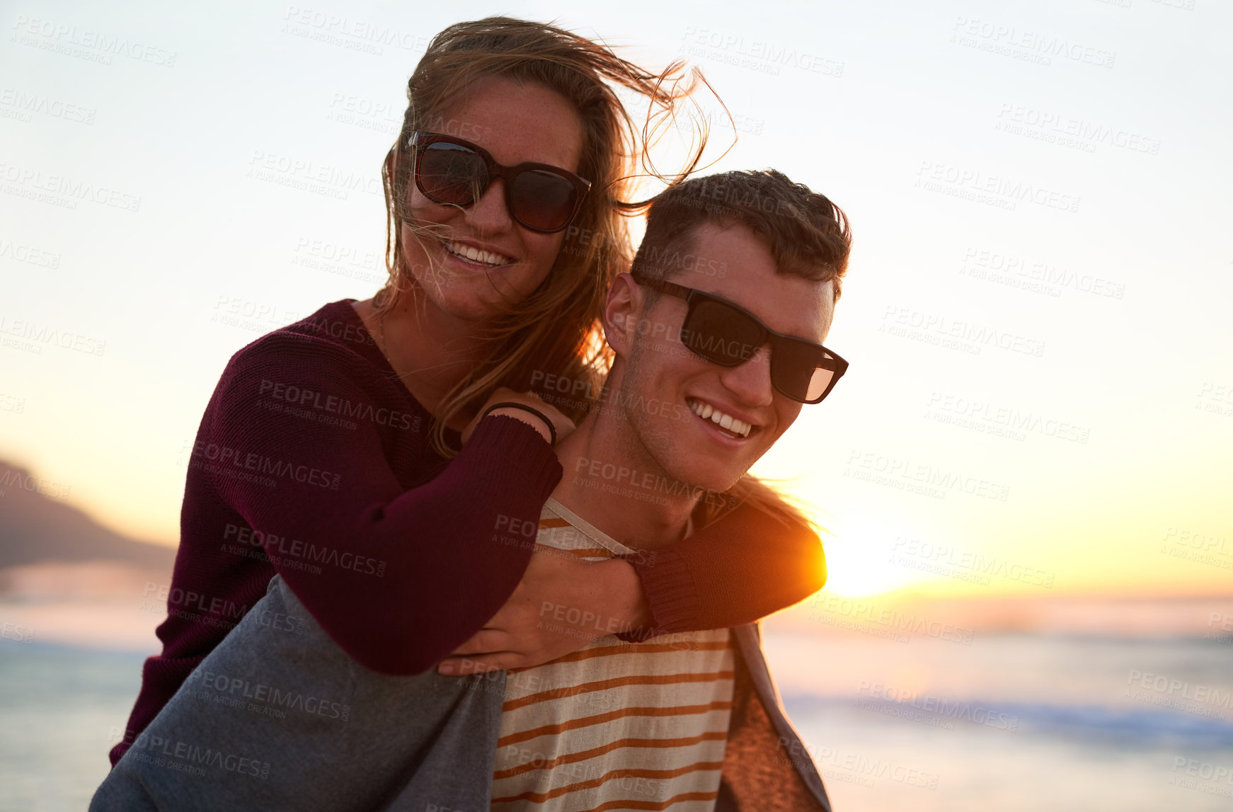 Buy stock photo Cropped portrait of an affectionate young man piggybacking his girlfriend at the beach