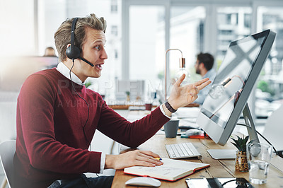 Buy stock photo Shot of a young man using a headset and computer in a modern office