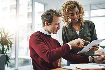 Buy stock photo Shot of two young colleagues using a digital tablet together in a modern office