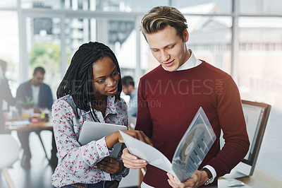 Buy stock photo Shot of two young colleagues discussing paperwork together in a modern office