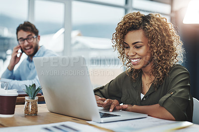 Buy stock photo Shot of a young woman working at her desk with her colleague in the background
