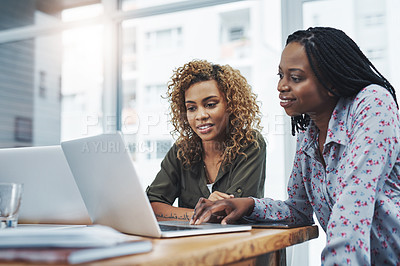 Buy stock photo Shot of two young colleagues using a laptop together in a modern office