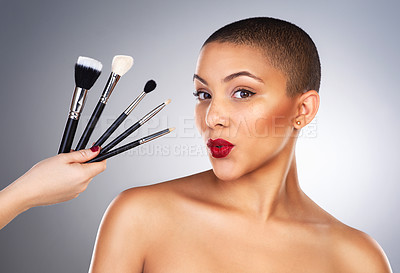 Buy stock photo Studio shot of a hand holding makeup brushes next to a beautiful young woman's face