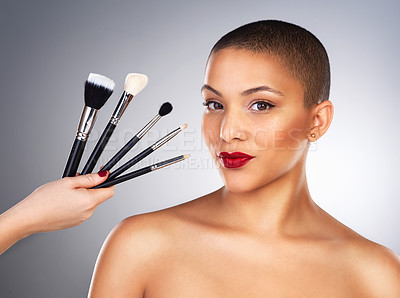 Buy stock photo Studio shot of a hand holding makeup brushes next to a beautiful young woman's face