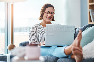 Buy stock photo Full length shot of a happy young woman using a laptop while relaxing in her living room