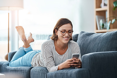 Buy stock photo Full length shot of a happy young woman using her smartphone on the sofa at home