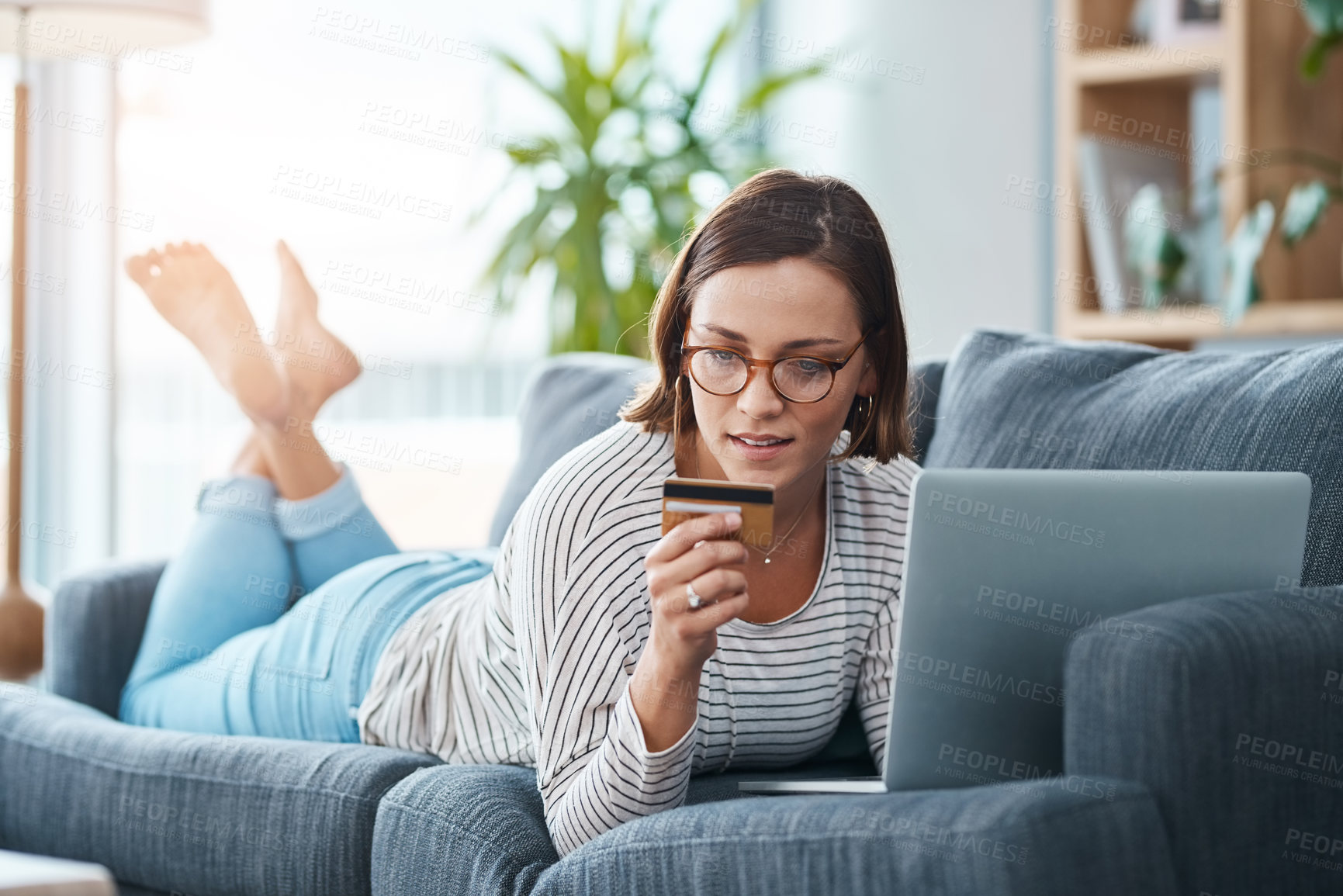 Buy stock photo Full length shot of a young woman using her laptop and credit card on the sofa at home