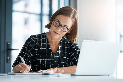 Buy stock photo Cropped shot of a focused young businesswoman writing on a notebook in an office
