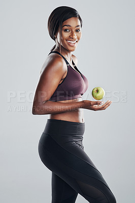 Buy stock photo Studio portrait of an attractive and fit young woman posing with an apple in her hand against a grey background