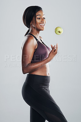 Buy stock photo Studio shot of an attractive and fit young woman throwing an apple in the air against a grey background