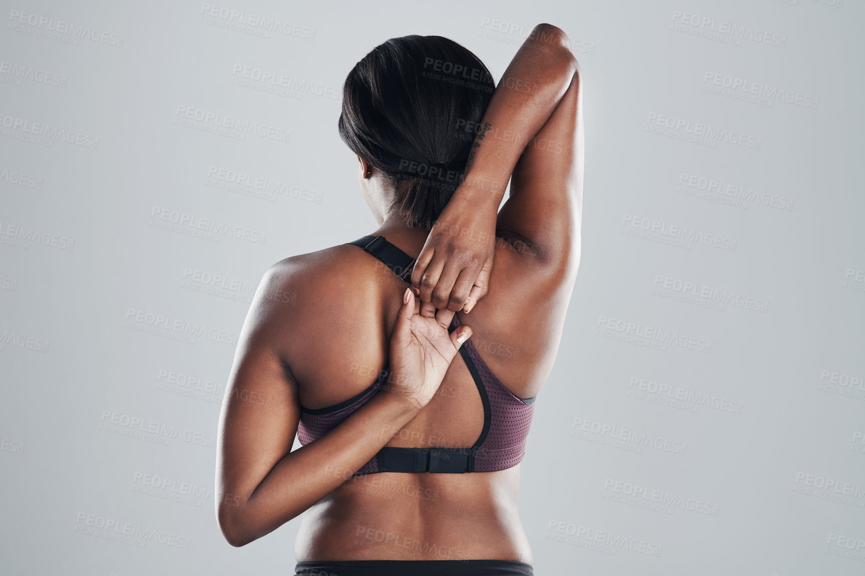 Buy stock photo Rearview shot of an athletic young woman stretching her arms against a grey background